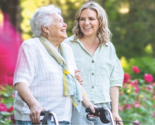 Una signora anziana e una giovane accompagnatrice sorridono insieme in giardino